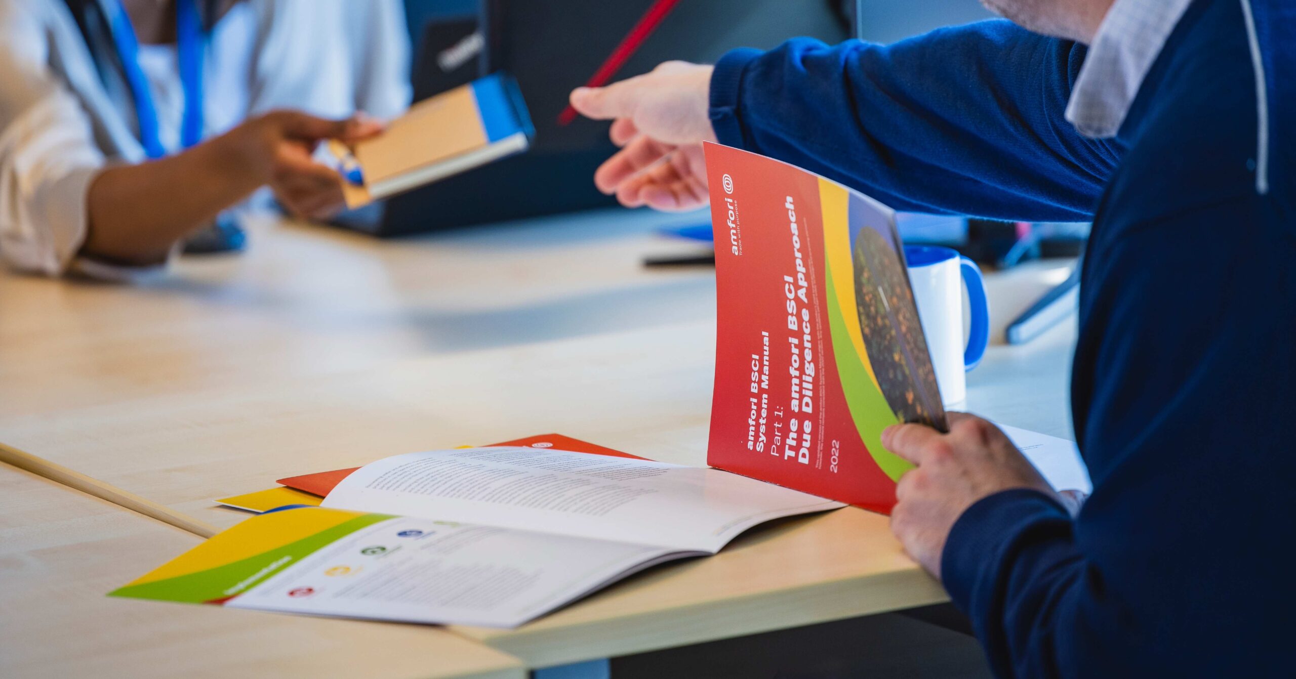 Two people are sitting facing each other at a table, one person is holding a red document in their hand.