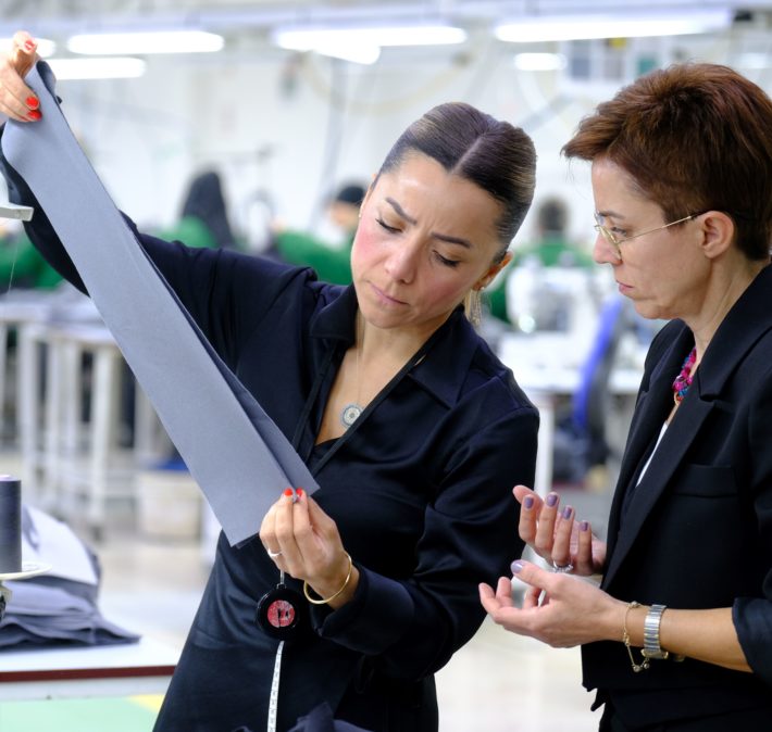 two women looking at a piece of fabric in a factory