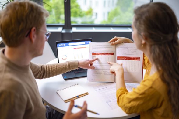 A man and a woman point at a document showing a table with numbers.