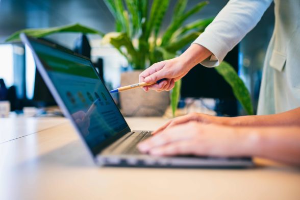 A person is using the keyboard of a laptop while another one is pointing at the screen.