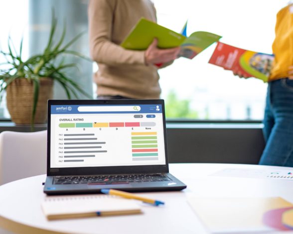 A laptop screen showing audit ratings and two people standing in the background.