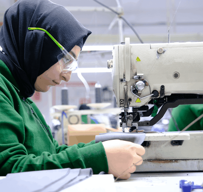 A female worker wearing protection glasses is sewing a piece of grey material